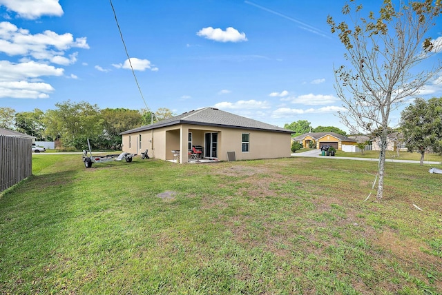 back of house featuring fence, a lawn, and stucco siding