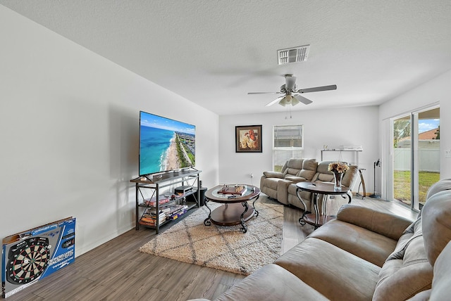 living area featuring baseboards, a textured ceiling, visible vents, and wood finished floors