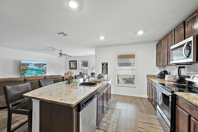 kitchen featuring a kitchen island, a sink, dark brown cabinets, appliances with stainless steel finishes, and light wood-type flooring