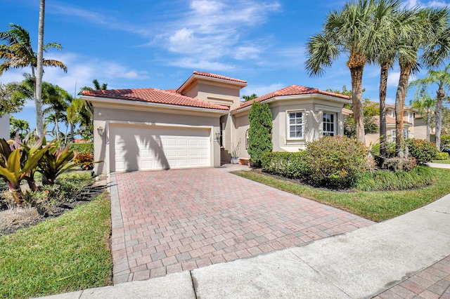 mediterranean / spanish house featuring an attached garage, a tiled roof, decorative driveway, and stucco siding