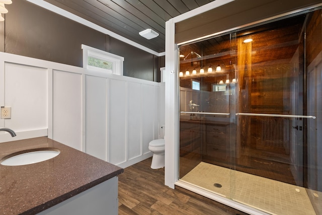 full bathroom with toilet, a decorative wall, wood finished floors, vanity, and a shower stall