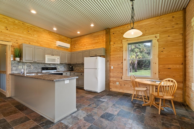 kitchen with dark countertops, hanging light fixtures, a sink, white appliances, and a peninsula