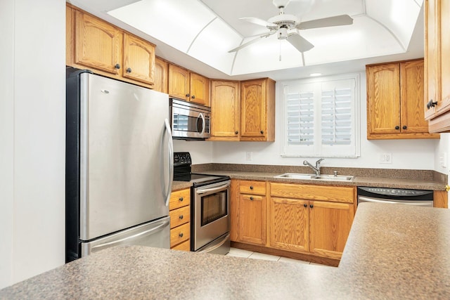 kitchen featuring a ceiling fan, a tray ceiling, stainless steel appliances, and a sink