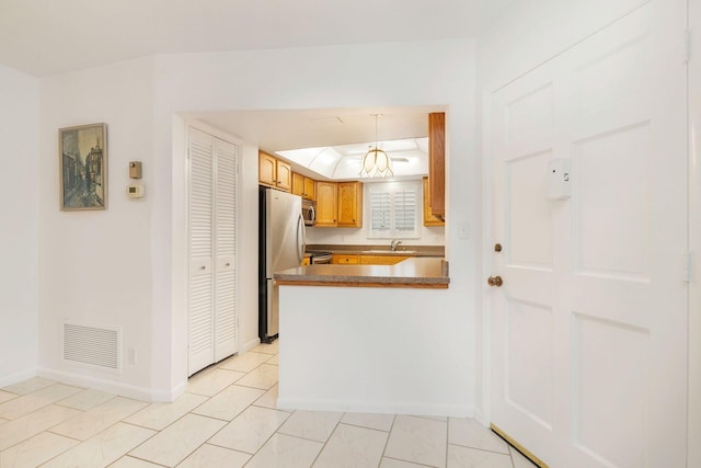 kitchen featuring a tray ceiling, visible vents, appliances with stainless steel finishes, a peninsula, and baseboards