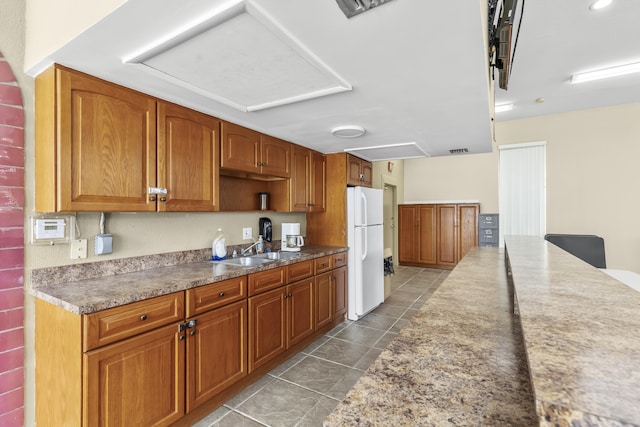 kitchen with visible vents, brown cabinetry, freestanding refrigerator, tile patterned flooring, and a sink