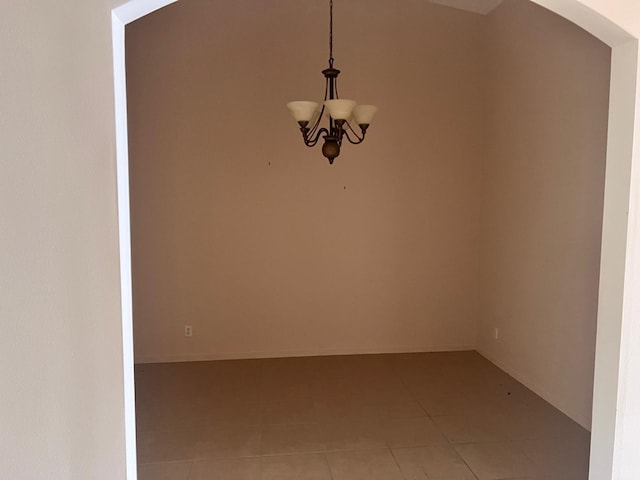 tiled spare room featuring a notable chandelier