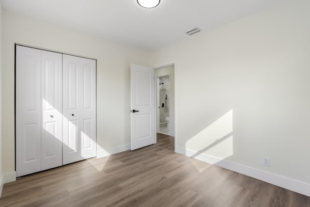 unfurnished bedroom featuring baseboards, a closet, visible vents, and wood finished floors