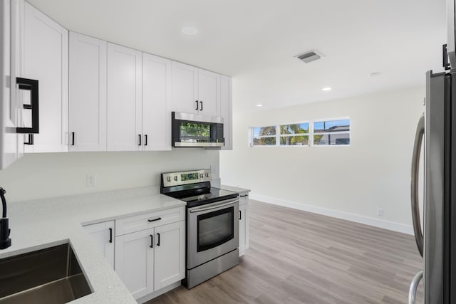 kitchen with stainless steel appliances, visible vents, light wood-style floors, white cabinetry, and light stone countertops