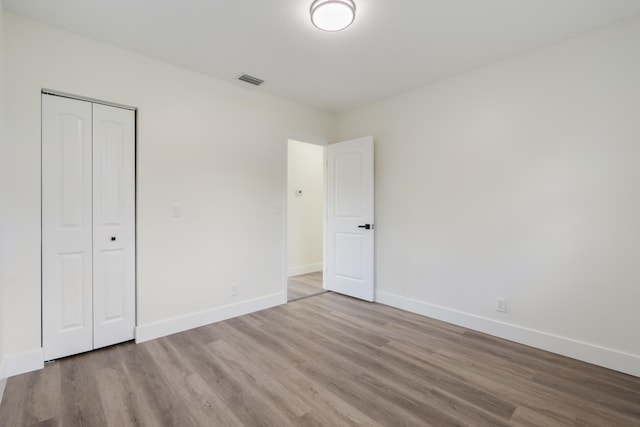 unfurnished bedroom featuring visible vents, a closet, light wood-style flooring, and baseboards