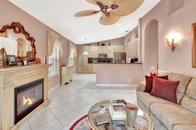 living room featuring light tile patterned floors, baseboards, a glass covered fireplace, ceiling fan, and vaulted ceiling