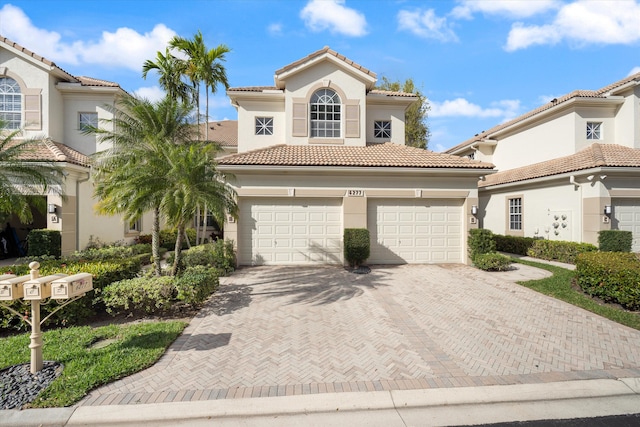 mediterranean / spanish house featuring a garage, a tiled roof, decorative driveway, and stucco siding