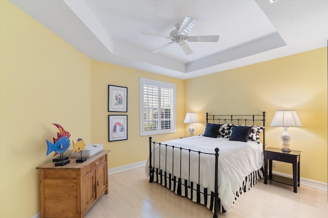 bedroom featuring baseboards, ceiling fan, a raised ceiling, and light wood-style floors