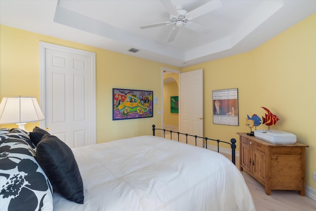 bedroom with ceiling fan, light wood-type flooring, a raised ceiling, and baseboards