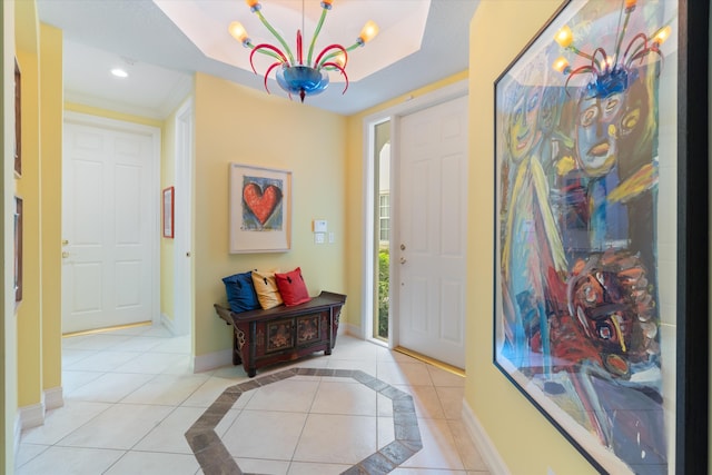 foyer entrance with a chandelier, a tray ceiling, tile patterned flooring, and baseboards