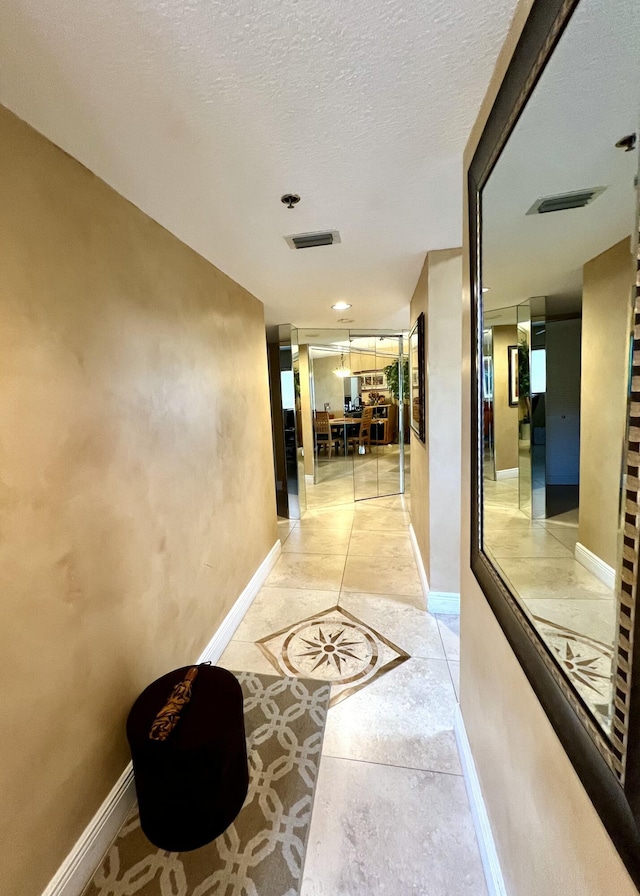 corridor featuring visible vents, a textured ceiling, and baseboards