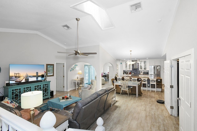 living room featuring arched walkways, visible vents, vaulted ceiling, and light wood finished floors