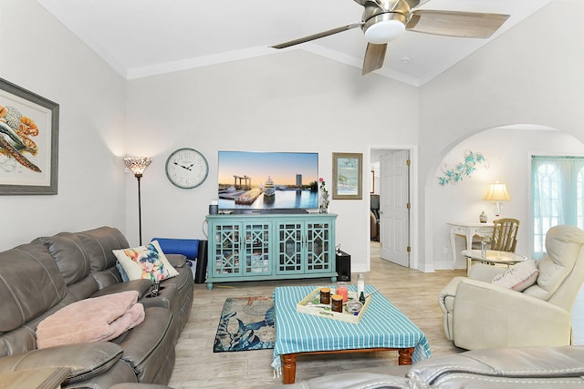 living area with arched walkways, baseboards, ceiling fan, light wood-style flooring, and vaulted ceiling