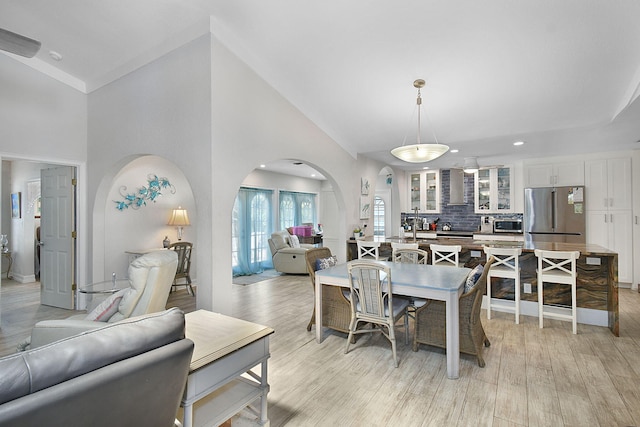 dining space featuring arched walkways, light wood finished floors, lofted ceiling, and recessed lighting