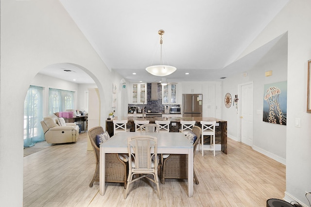 dining area with arched walkways, lofted ceiling, recessed lighting, baseboards, and light wood-type flooring