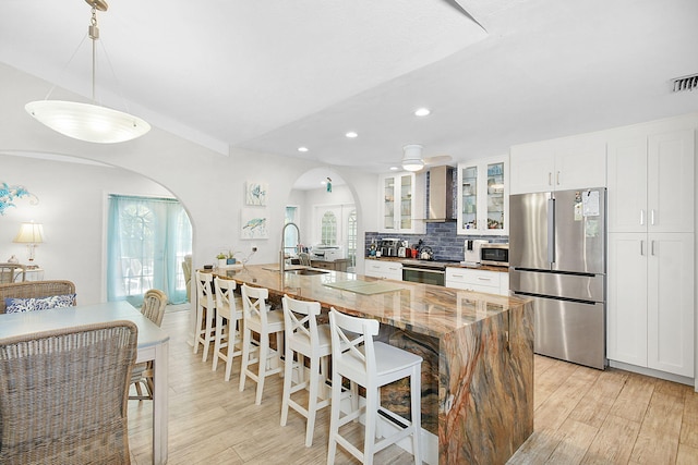 kitchen with glass insert cabinets, appliances with stainless steel finishes, wall chimney range hood, white cabinetry, and a sink