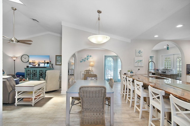 dining area featuring arched walkways, vaulted ceiling, light wood-type flooring, and a healthy amount of sunlight