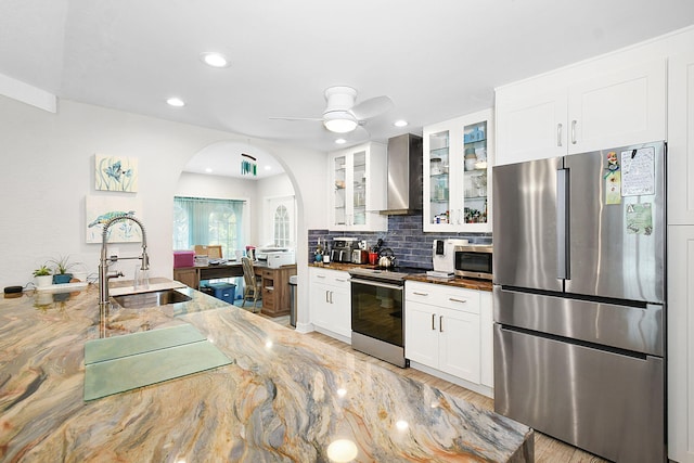 kitchen with appliances with stainless steel finishes, glass insert cabinets, white cabinets, a sink, and wall chimney exhaust hood