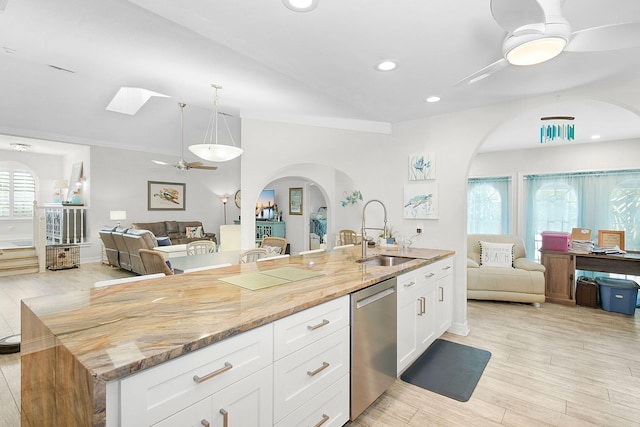 kitchen featuring open floor plan, stainless steel dishwasher, a sink, and white cabinetry