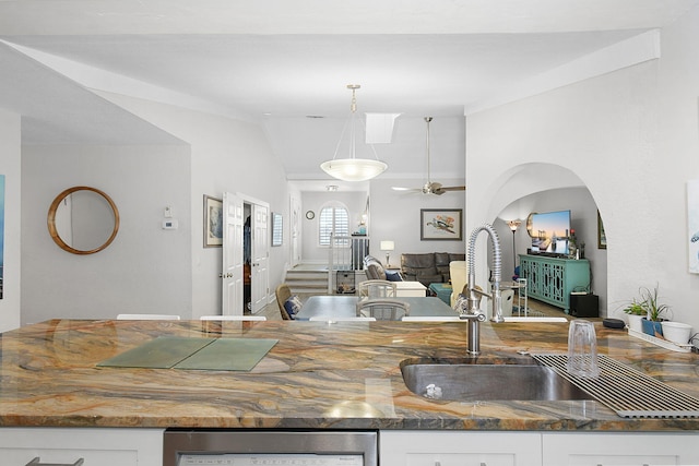 kitchen with hanging light fixtures, white cabinets, vaulted ceiling, a sink, and dishwasher