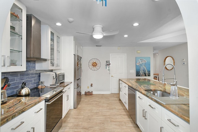 kitchen featuring white cabinets, dark stone counters, glass insert cabinets, appliances with stainless steel finishes, and wall chimney range hood