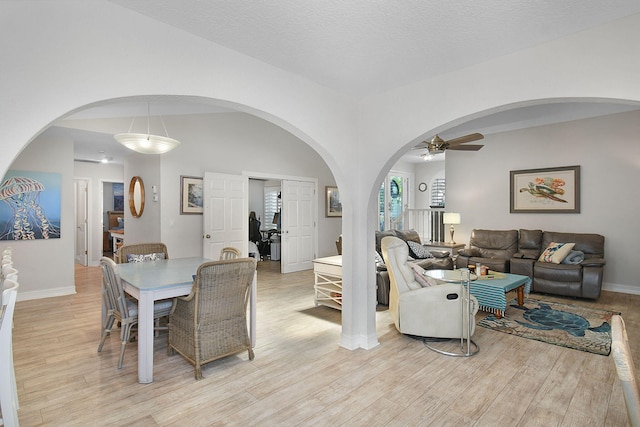 dining space with arched walkways, light wood-type flooring, a ceiling fan, and baseboards