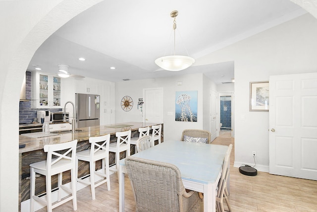 dining area with arched walkways, lofted ceiling, light wood-style flooring, ceiling fan, and baseboards