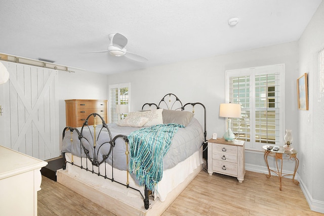 bedroom featuring visible vents, light wood-style flooring, a barn door, ceiling fan, and a textured ceiling