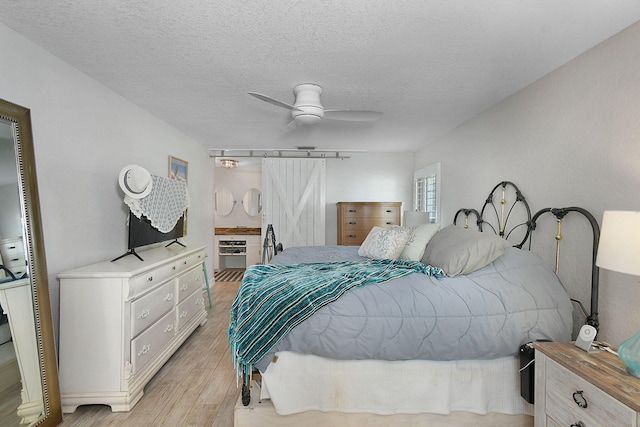 bedroom with a textured ceiling, a barn door, light wood-type flooring, and a ceiling fan