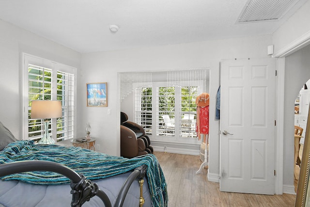 bedroom featuring light wood-style flooring, visible vents, arched walkways, and baseboards