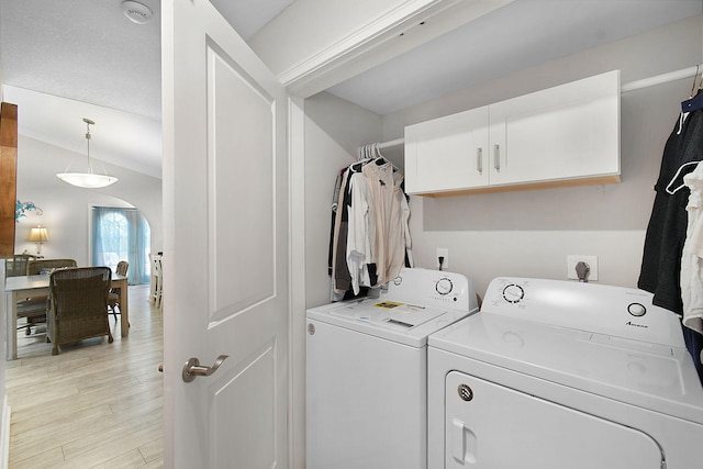 laundry room featuring arched walkways, laundry area, washing machine and dryer, and light wood-style floors