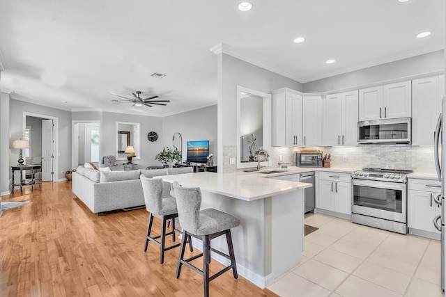 kitchen featuring white cabinets, appliances with stainless steel finishes, open floor plan, a peninsula, and a kitchen bar