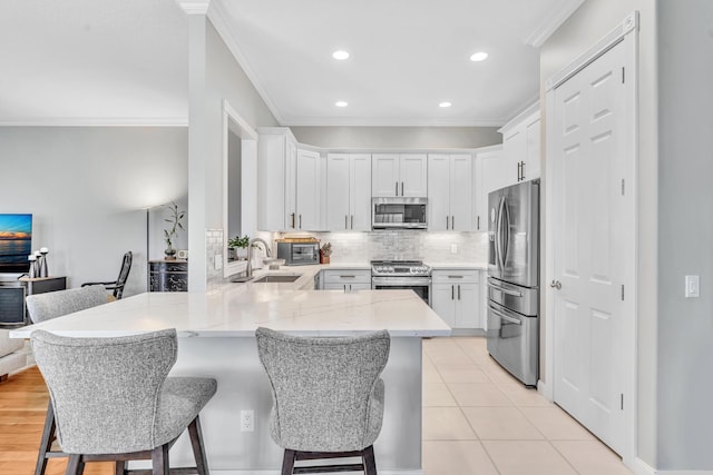 kitchen with white cabinets, a breakfast bar area, a peninsula, stainless steel appliances, and a sink