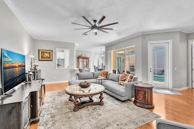 living room with baseboards, light wood-style flooring, ornamental molding, a textured ceiling, and ceiling fan with notable chandelier