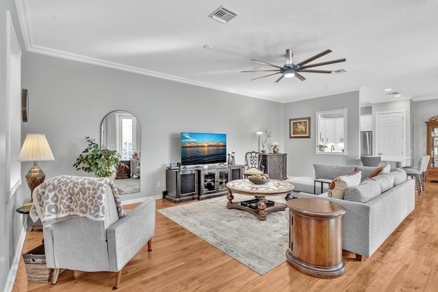 living room featuring crown molding, light wood finished floors, visible vents, a ceiling fan, and a textured ceiling