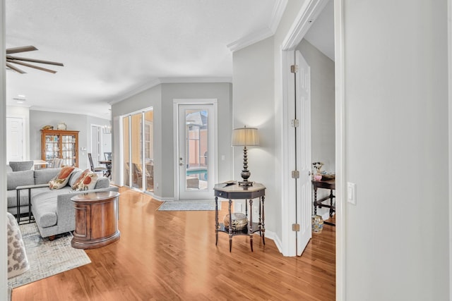 living room featuring a ceiling fan, crown molding, baseboards, and wood finished floors