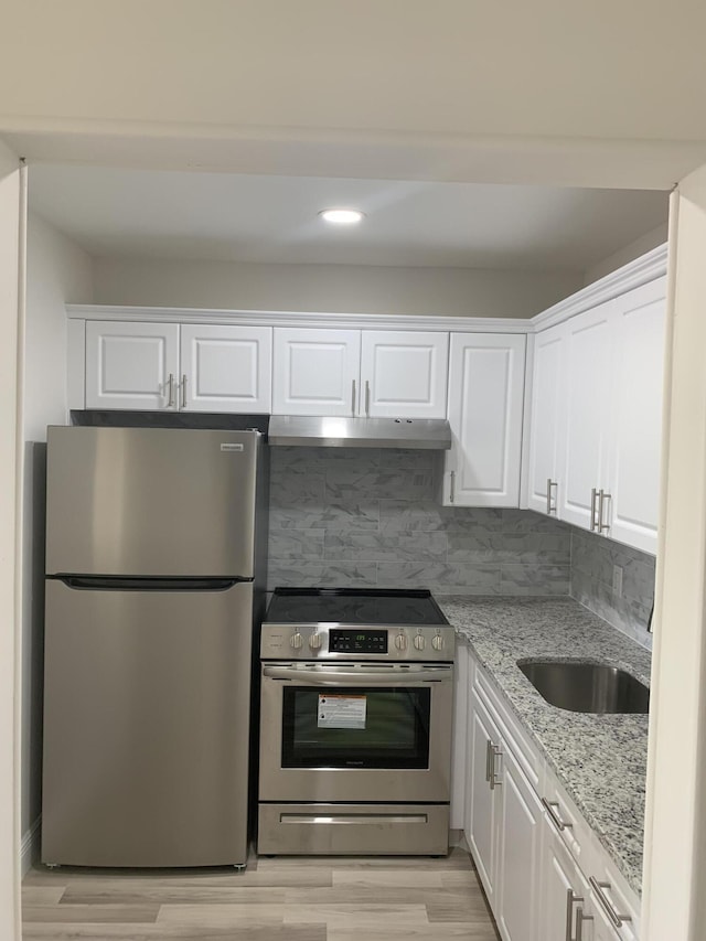 kitchen with white cabinets, light stone counters, stainless steel appliances, light wood-type flooring, and under cabinet range hood