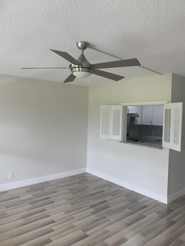 spare room featuring a textured ceiling, light wood finished floors, a ceiling fan, and baseboards