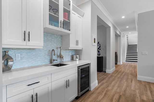 kitchen with glass insert cabinets, wine cooler, light wood-type flooring, light countertops, and a sink