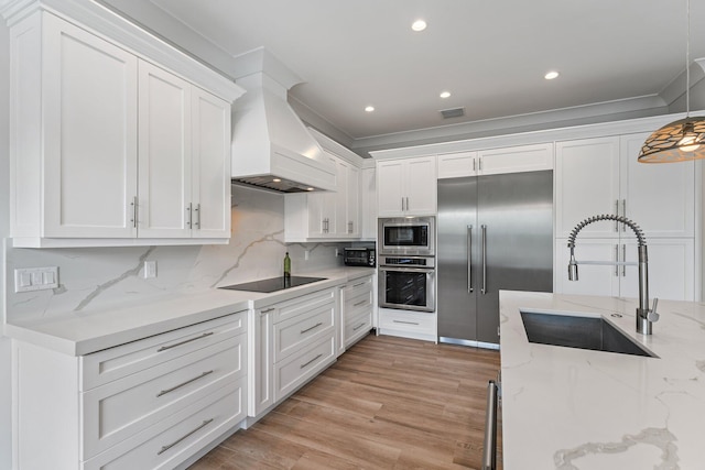 kitchen featuring white cabinetry, custom range hood, built in appliances, and a sink