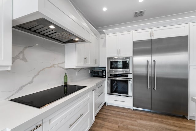 kitchen with premium range hood, built in appliances, white cabinets, and wood finished floors