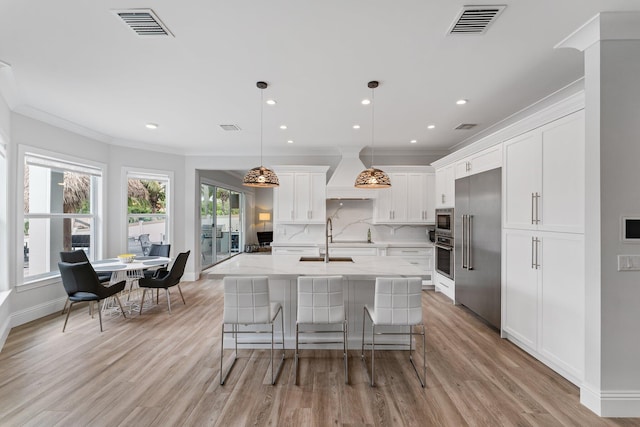 kitchen with custom exhaust hood, built in appliances, visible vents, and a sink