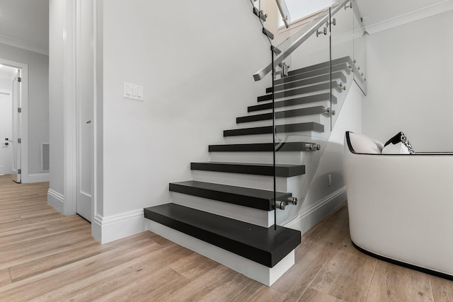 staircase featuring crown molding, wood finished floors, visible vents, and baseboards