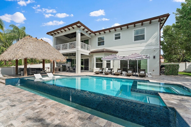 rear view of house with a patio, a balcony, a pool with connected hot tub, and fence