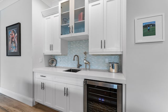 bar featuring wood finished floors, beverage cooler, baseboards, a sink, and decorative backsplash