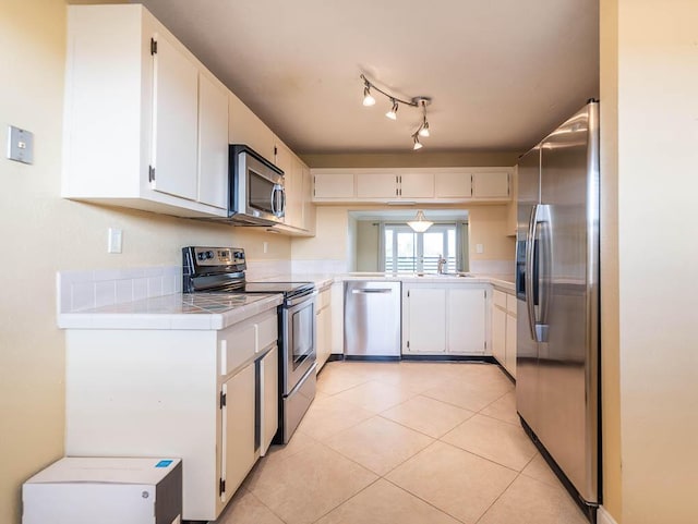 kitchen featuring tile countertops, stainless steel appliances, white cabinetry, a sink, and light tile patterned flooring